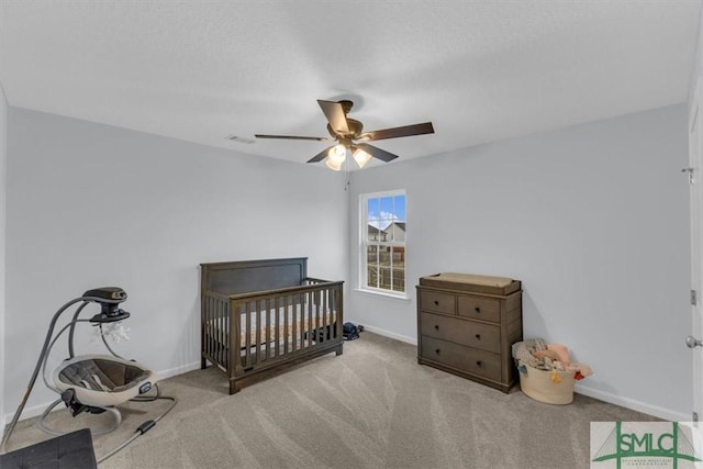 bedroom with a nursery area, light colored carpet, and ceiling fan