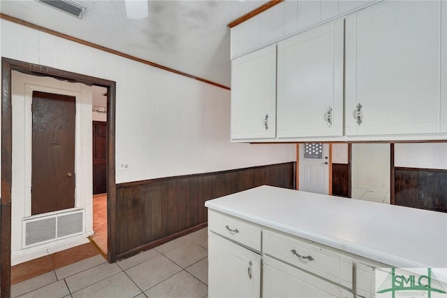 kitchen featuring a textured ceiling, light tile patterned flooring, ornamental molding, and white cabinetry