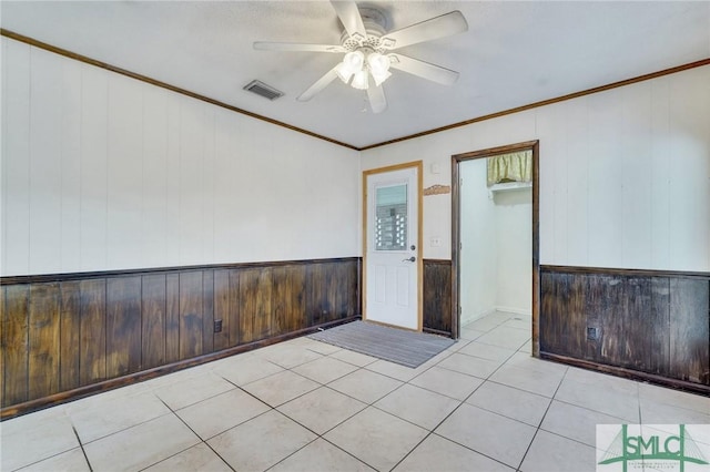 empty room with ornamental molding, ceiling fan, light tile patterned flooring, and wood walls