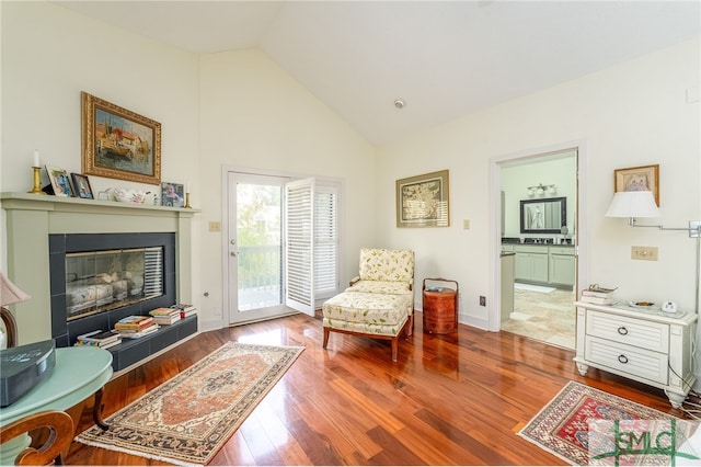 sitting room featuring high vaulted ceiling, a tiled fireplace, and hardwood / wood-style flooring