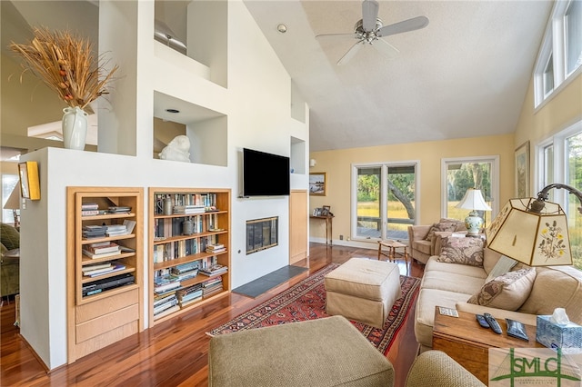 living room with a high ceiling, a fireplace, ceiling fan, and dark hardwood / wood-style floors