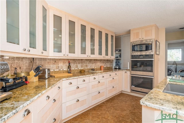 kitchen featuring stainless steel appliances, a textured ceiling, sink, washer and clothes dryer, and tasteful backsplash