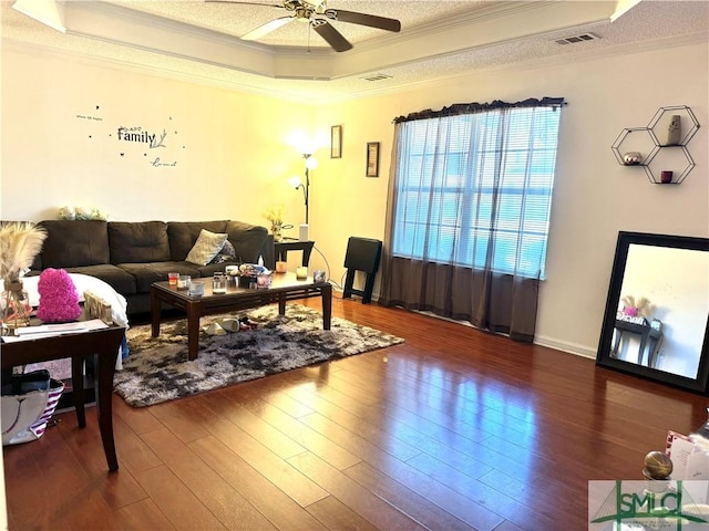 living room with ornamental molding, dark wood-type flooring, ceiling fan, and a tray ceiling