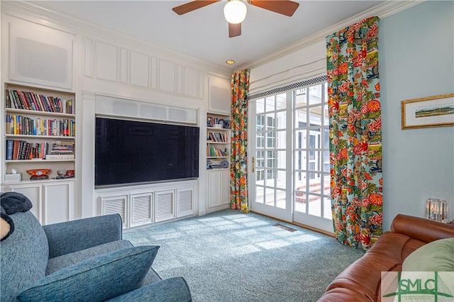 carpeted living room featuring built in shelves, ceiling fan, and ornamental molding