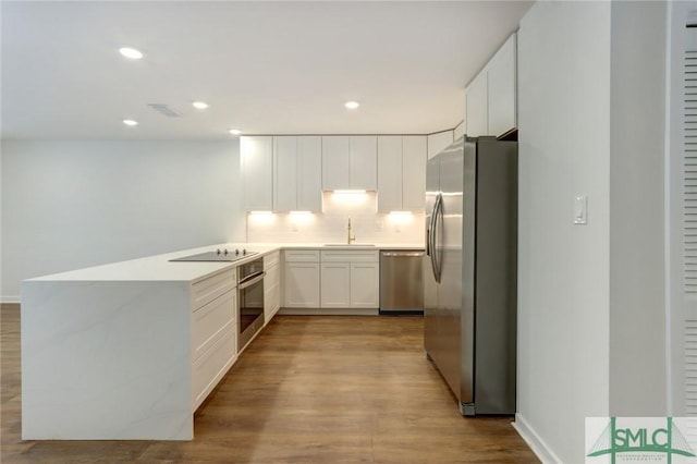 kitchen featuring stainless steel appliances, decorative backsplash, white cabinets, light hardwood / wood-style flooring, and sink