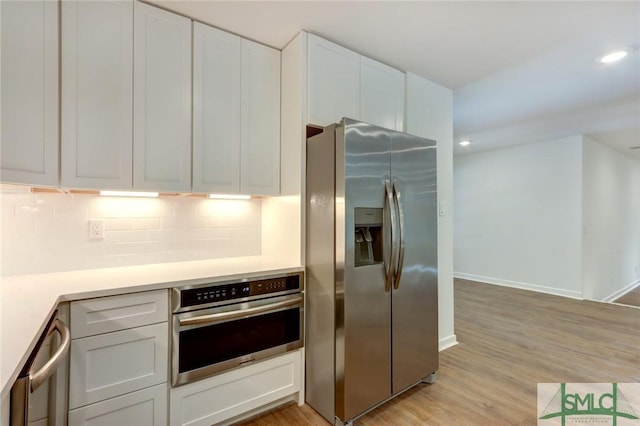 kitchen featuring white cabinetry, tasteful backsplash, light hardwood / wood-style floors, and appliances with stainless steel finishes