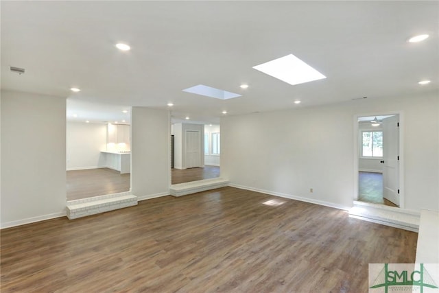 unfurnished living room featuring hardwood / wood-style flooring, ceiling fan, and a skylight