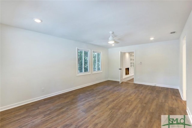 empty room featuring dark wood-type flooring, ceiling fan, and a brick fireplace