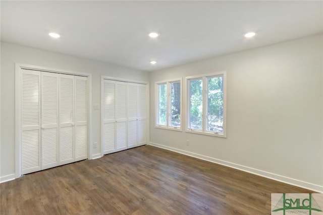 unfurnished bedroom with multiple closets and dark wood-type flooring