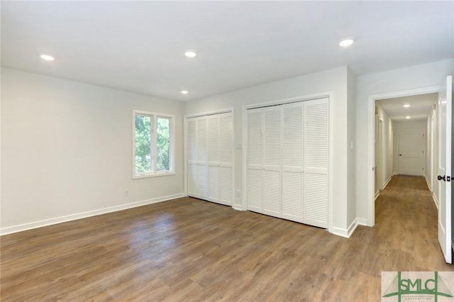 unfurnished bedroom with multiple closets and wood-type flooring