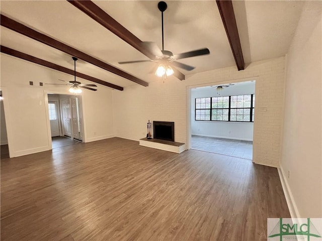 unfurnished living room with ceiling fan, dark hardwood / wood-style floors, a brick fireplace, and beamed ceiling