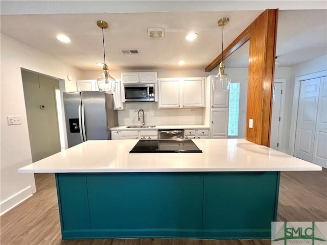 kitchen with decorative light fixtures, hardwood / wood-style floors, white cabinets, appliances with stainless steel finishes, and sink