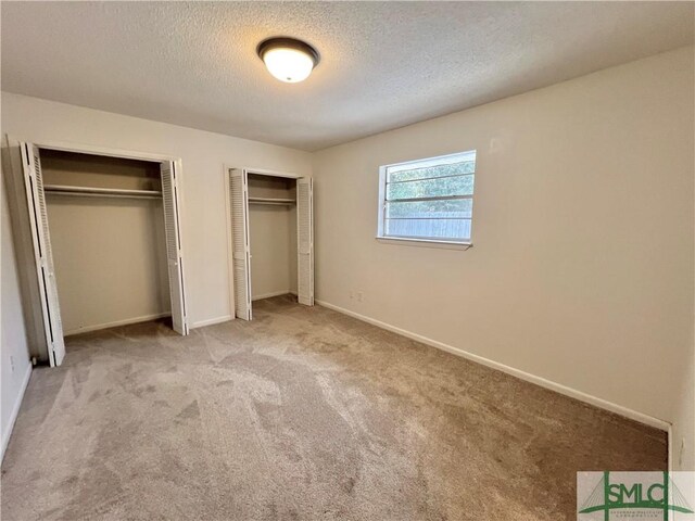 unfurnished bedroom with two closets, light carpet, and a textured ceiling