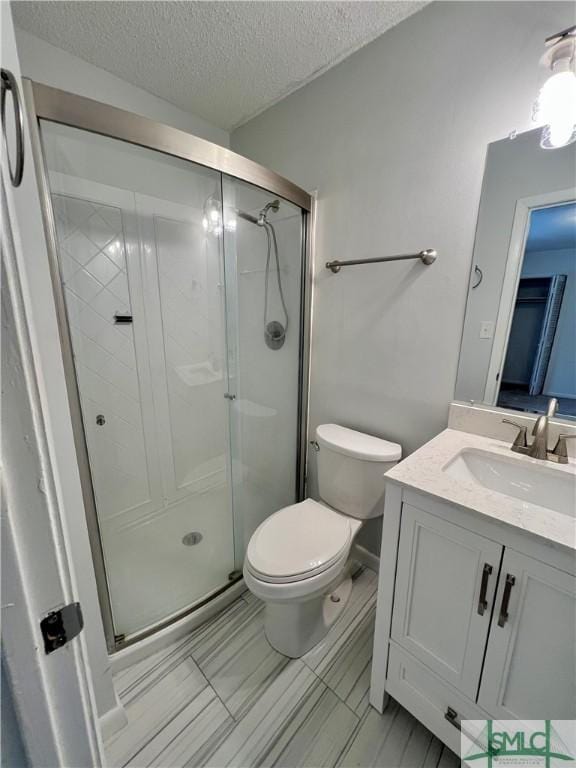 bathroom featuring toilet, a shower with door, vanity, and a textured ceiling