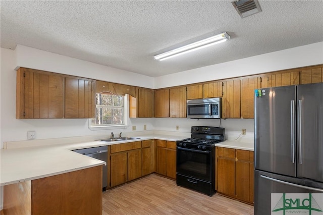 kitchen featuring kitchen peninsula, a textured ceiling, appliances with stainless steel finishes, and light hardwood / wood-style flooring