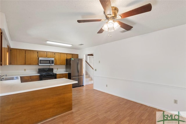 kitchen featuring sink, light wood-type flooring, ceiling fan, kitchen peninsula, and appliances with stainless steel finishes