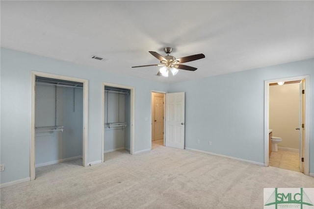 unfurnished bedroom with two closets, ceiling fan, light carpet, and connected bathroom