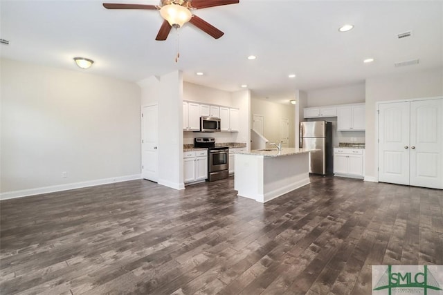 kitchen with appliances with stainless steel finishes, white cabinets, light stone counters, a kitchen island with sink, and dark wood-type flooring