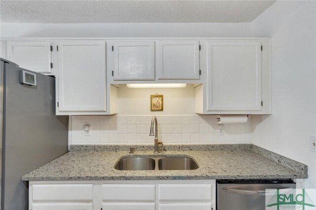 kitchen with sink, appliances with stainless steel finishes, white cabinetry, backsplash, and light stone countertops