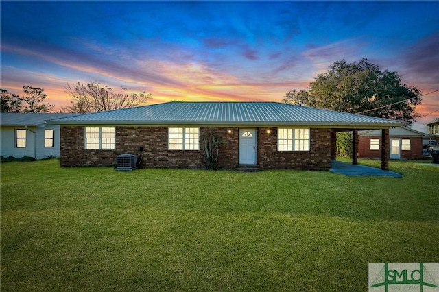 back house at dusk with central AC, a lawn, and a carport