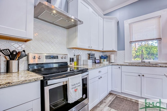 kitchen featuring light stone countertops, wall chimney exhaust hood, stainless steel range with electric cooktop, white cabinetry, and sink