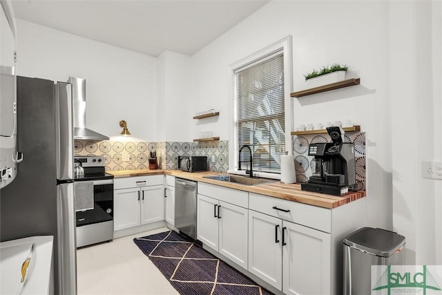 kitchen featuring sink, stainless steel appliances, white cabinetry, wall chimney exhaust hood, and wood counters