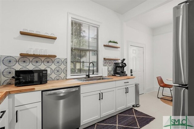 kitchen with appliances with stainless steel finishes, a healthy amount of sunlight, butcher block countertops, sink, and white cabinetry