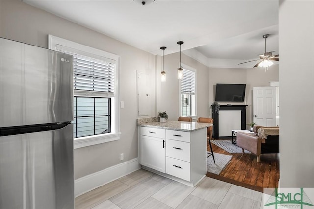 kitchen with light stone countertops, hanging light fixtures, white cabinetry, stainless steel refrigerator, and ceiling fan