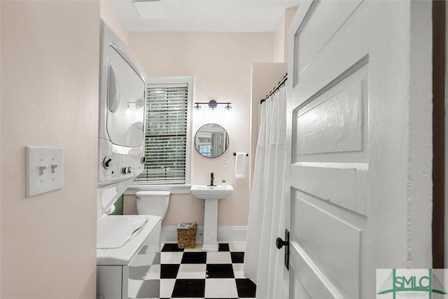 bathroom with toilet, a shower with curtain, and stacked washer / dryer