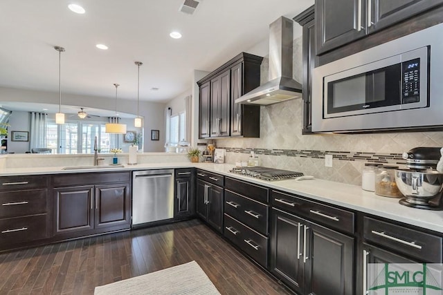 kitchen with appliances with stainless steel finishes, hanging light fixtures, kitchen peninsula, wall chimney exhaust hood, and sink