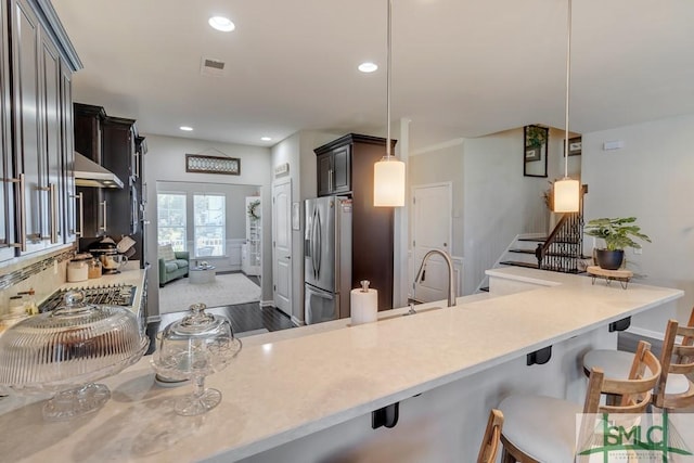 kitchen with kitchen peninsula, stainless steel fridge, pendant lighting, and a kitchen breakfast bar