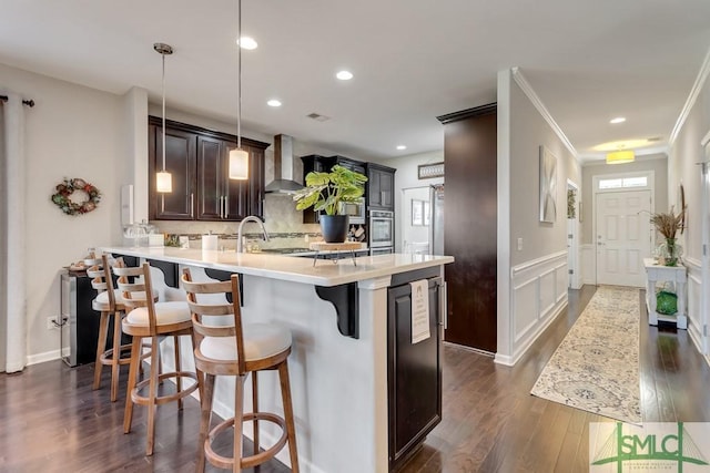 kitchen featuring kitchen peninsula, stainless steel oven, pendant lighting, wall chimney range hood, and a kitchen bar