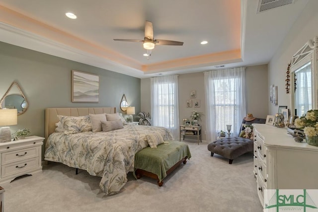 bedroom with ceiling fan, multiple windows, light carpet, and a raised ceiling