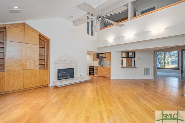 unfurnished living room with ceiling fan, light wood-type flooring, vaulted ceiling, a tile fireplace, and sink