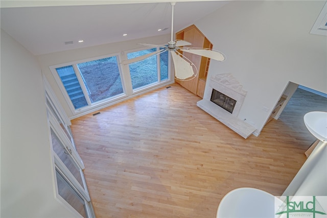 living room with vaulted ceiling, a premium fireplace, light hardwood / wood-style flooring, and ceiling fan