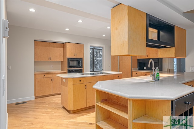 kitchen featuring kitchen peninsula, a center island, black appliances, light hardwood / wood-style flooring, and sink