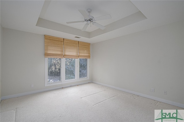 empty room with carpet floors, a raised ceiling, and ceiling fan