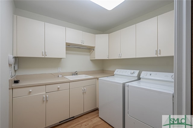 laundry room with washing machine and dryer, sink, light hardwood / wood-style floors, and cabinets