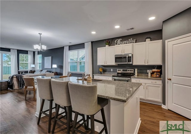 kitchen featuring appliances with stainless steel finishes, hanging light fixtures, white cabinetry, and a center island with sink