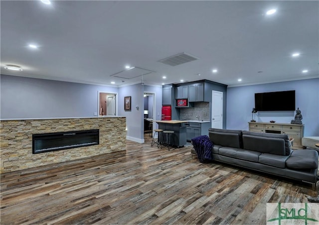 living room featuring dark hardwood / wood-style flooring, ornamental molding, and a stone fireplace