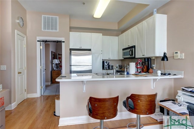 kitchen featuring kitchen peninsula, white cabinets, appliances with stainless steel finishes, and a kitchen bar