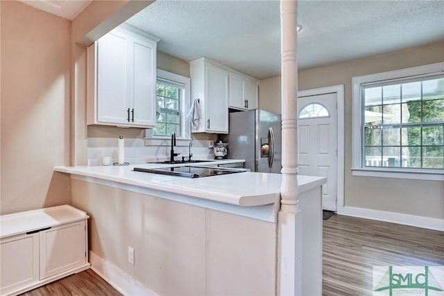 kitchen featuring kitchen peninsula, dark hardwood / wood-style floors, stainless steel refrigerator with ice dispenser, white cabinets, and sink