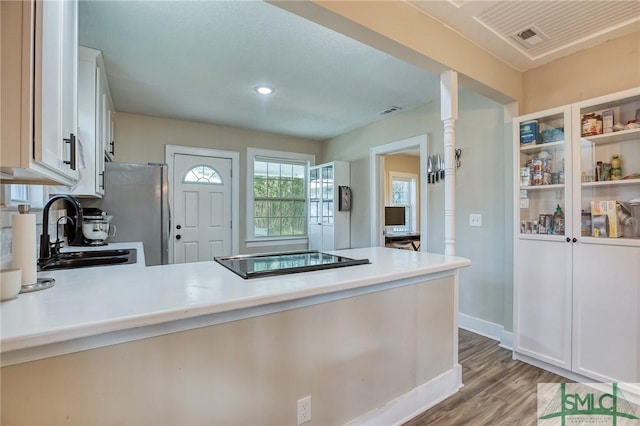 kitchen featuring stainless steel refrigerator, light hardwood / wood-style floors, black electric cooktop, sink, and white cabinetry