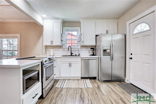 kitchen with sink, stainless steel appliances, light wood-type flooring, and white cabinets