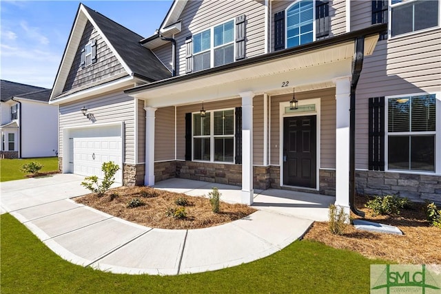 entrance to property featuring stone siding, a porch, driveway, and a garage