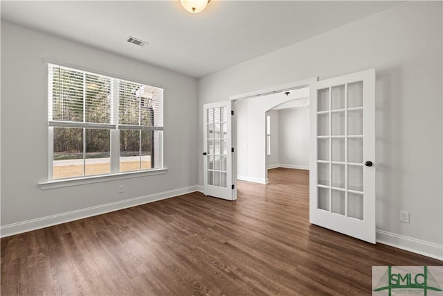 empty room with dark wood-style floors, visible vents, baseboards, arched walkways, and french doors