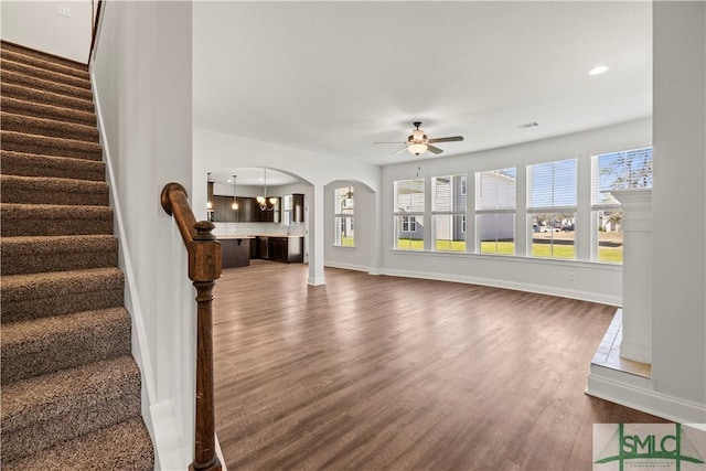 living area with a ceiling fan, dark wood-style floors, arched walkways, baseboards, and stairs