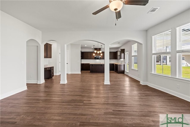 unfurnished living room with baseboards, visible vents, dark wood finished floors, arched walkways, and ceiling fan