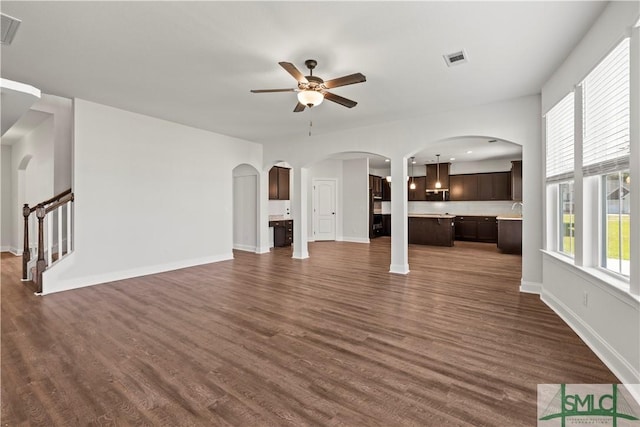 unfurnished living room featuring visible vents, baseboards, dark wood finished floors, arched walkways, and stairs