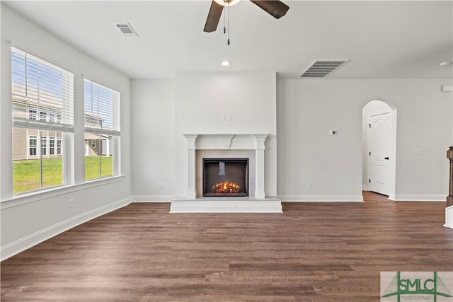 unfurnished living room with dark wood-type flooring, arched walkways, visible vents, and a lit fireplace